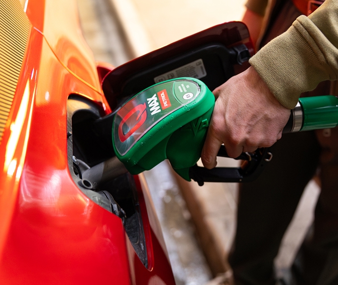 Ruka drži zelenu Q Max točilicu za gorivo umetnutu u spremnik crvenog automobila.