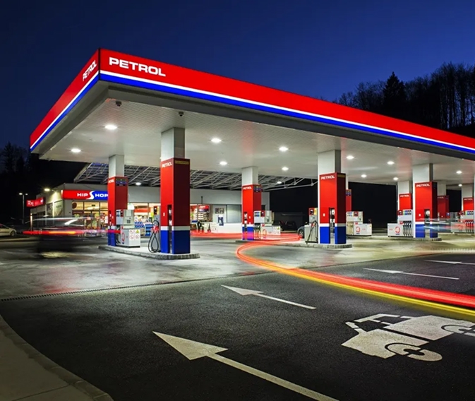 Petrolova benzinska stanica noću s osvetljenim točionicama, prodavnicom i svetlosnim tragovima vozila.