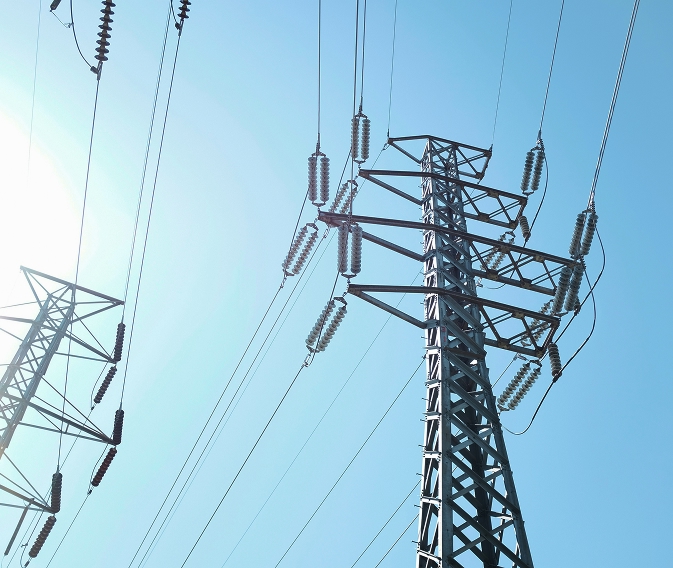 Dalekovodi i električni stupovi na vedrom nebu, obasjani sunčevom svjetlošću.