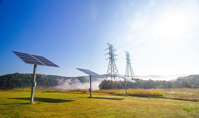 Na slici su solarni paneli i dalekovodi kao prikaz proizvodnje i prenosa električne energije.